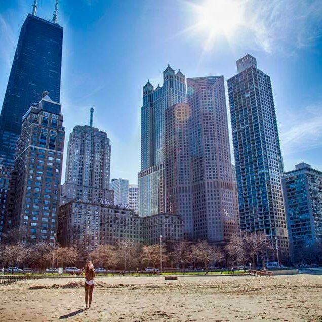 A picture of a person standing on a beach with skyscrapers in the background