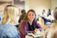 A student in a purple jacket smiles at her friend over lunch