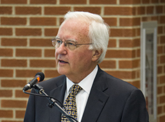 A man in a suit with glasses and white hair speaks into a microphone