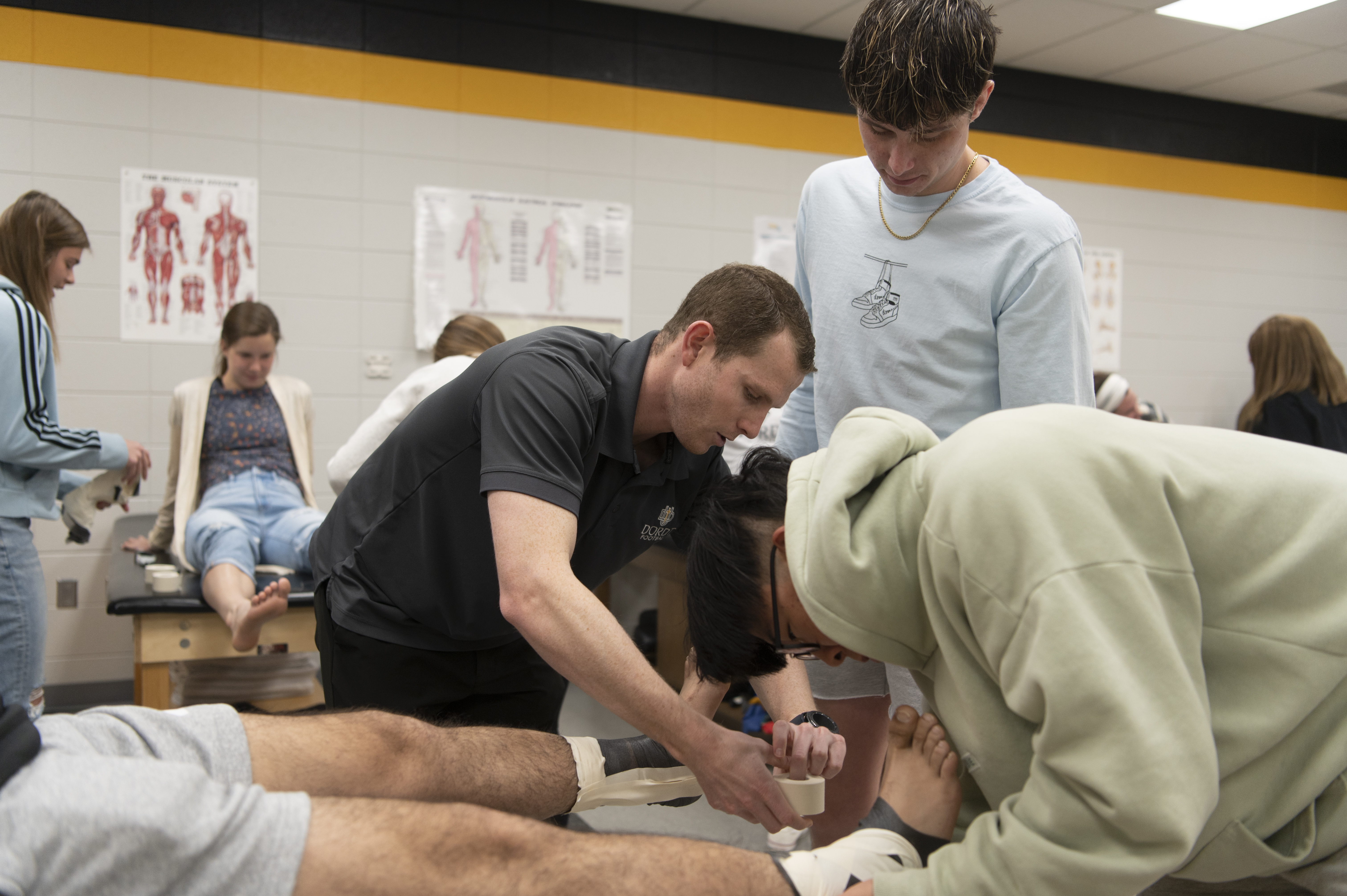 A professor/coach helps students tape ankles in the training room