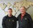 A picture of two men standing in front of a wall decoration of the world