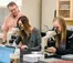 A picture of two ladies looking into microscopes while a professor looks at them