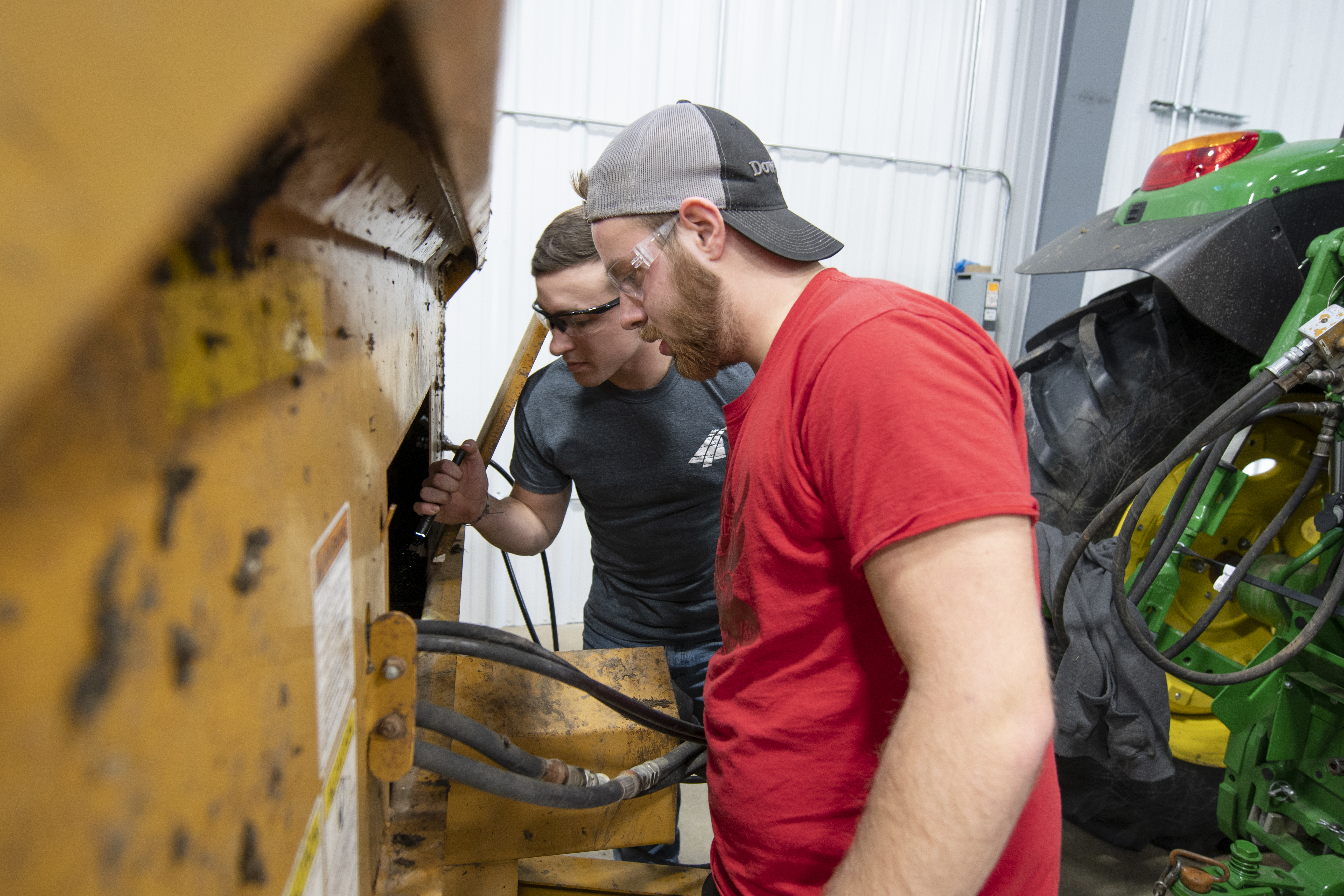 Two male students look into a manure spreader in ag maintenance class