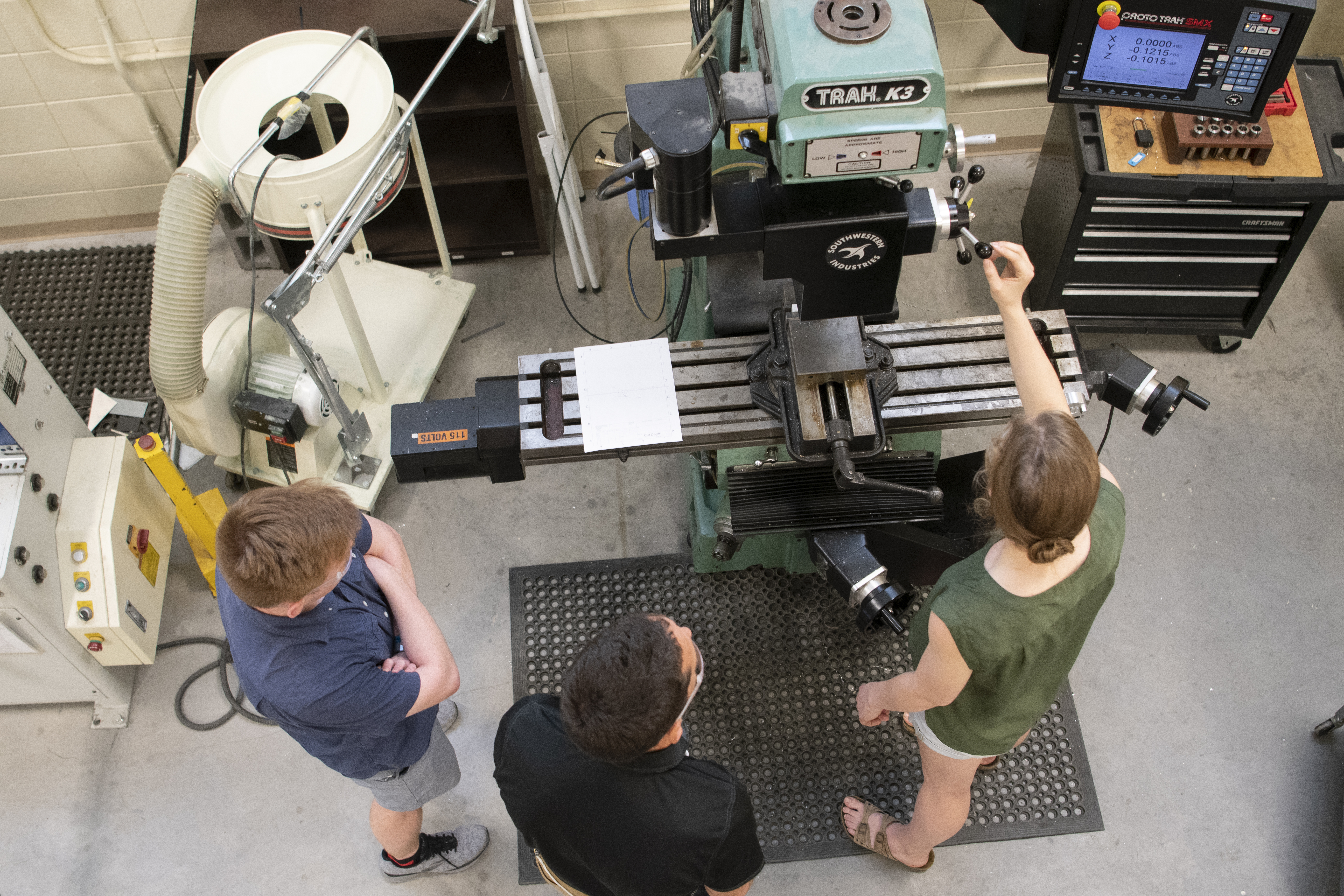 Two students and a faculty member work in a piece of equipment