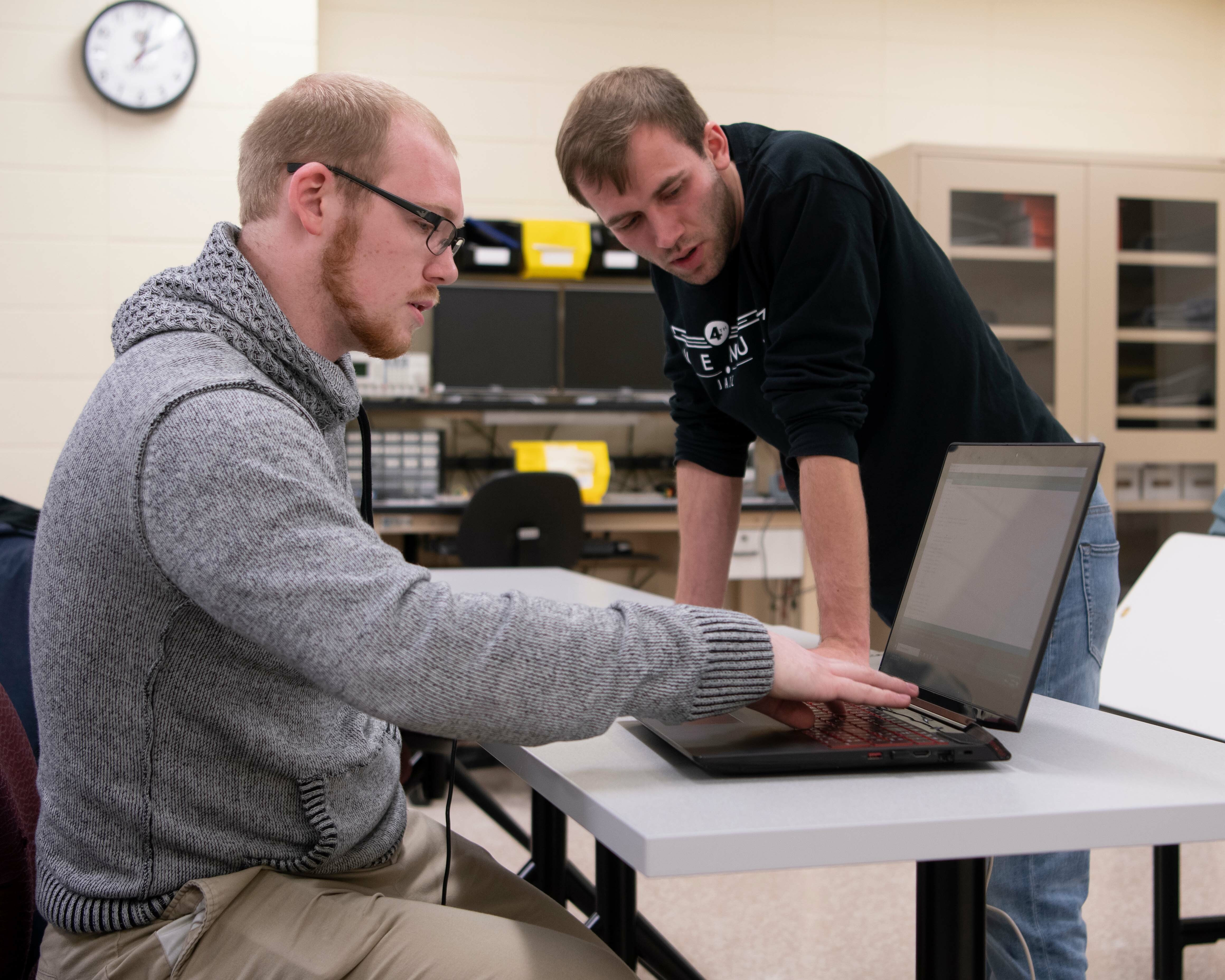 Two male students look at a laptop
