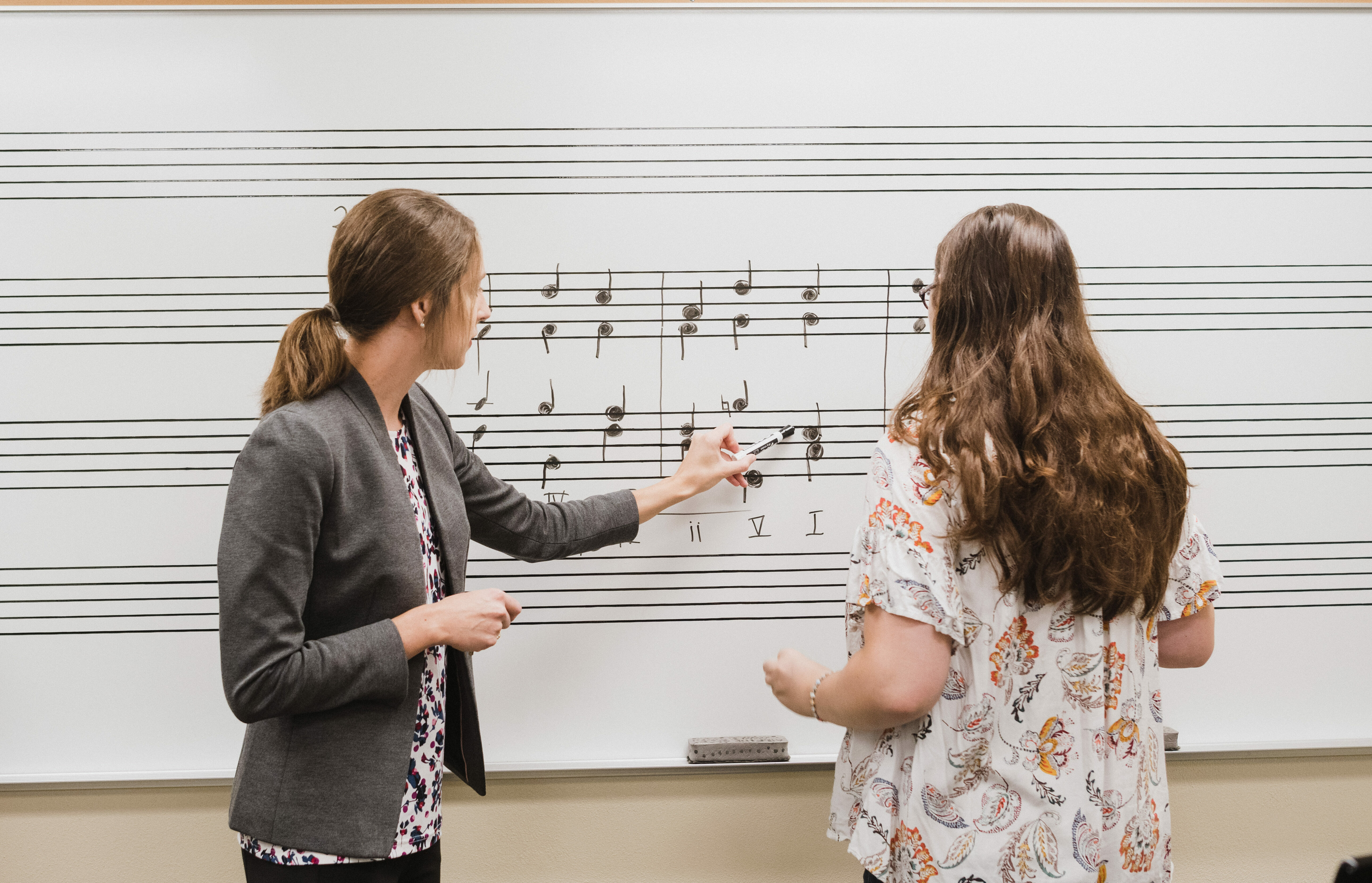Faculty member and student work out music notes on a whiteboard