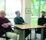 Three professors sit around a table looking at each other