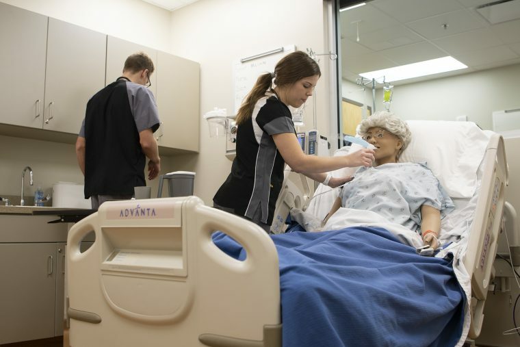 A student cares of a dummy in a nursing lab