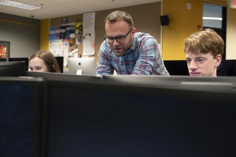 A picture of a professor helping students in a digital media lab
