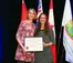 A picture of two women holding an award while standing in front of flags