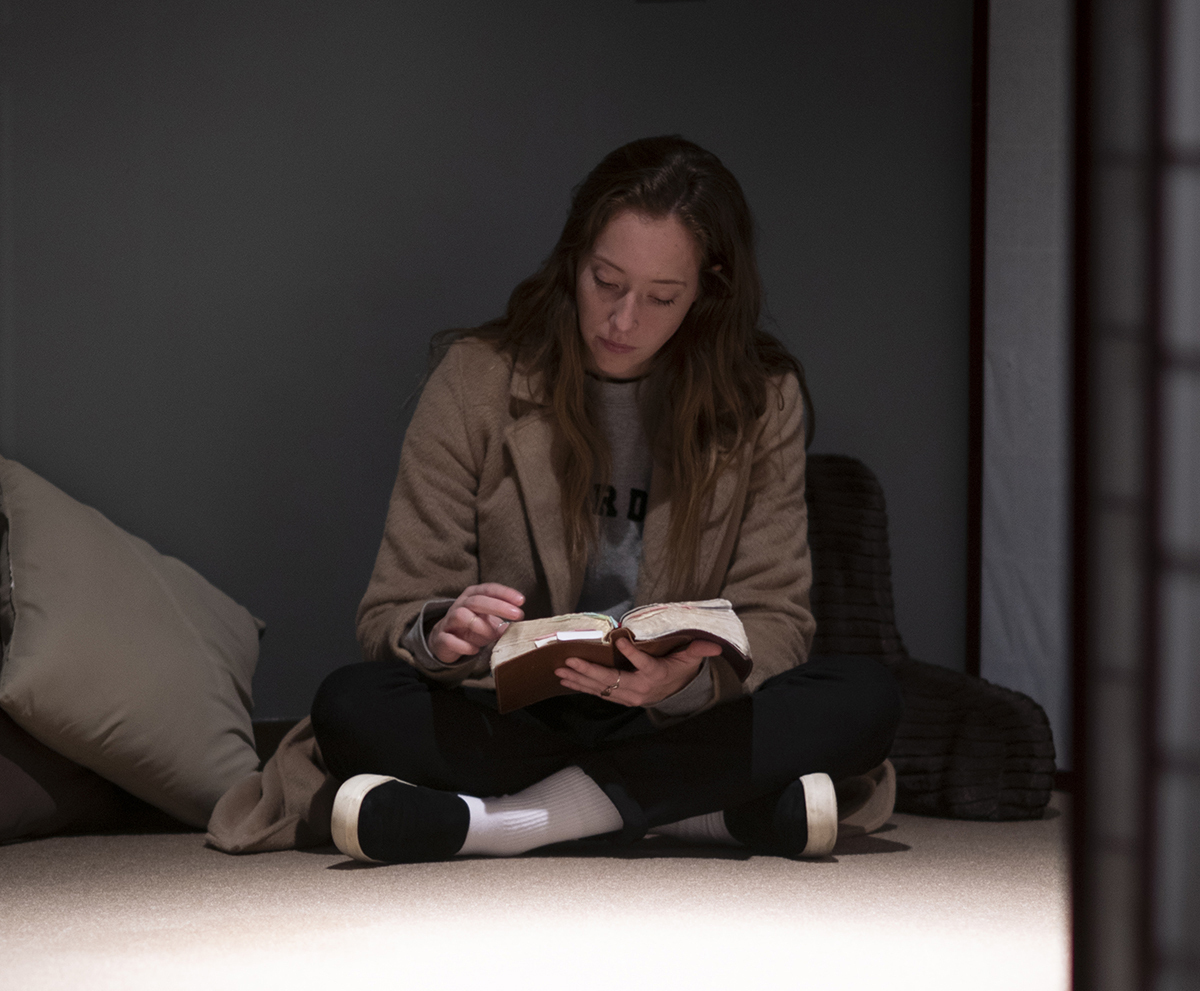 Female student sits pretzel-style on floor studying Bible in low light
