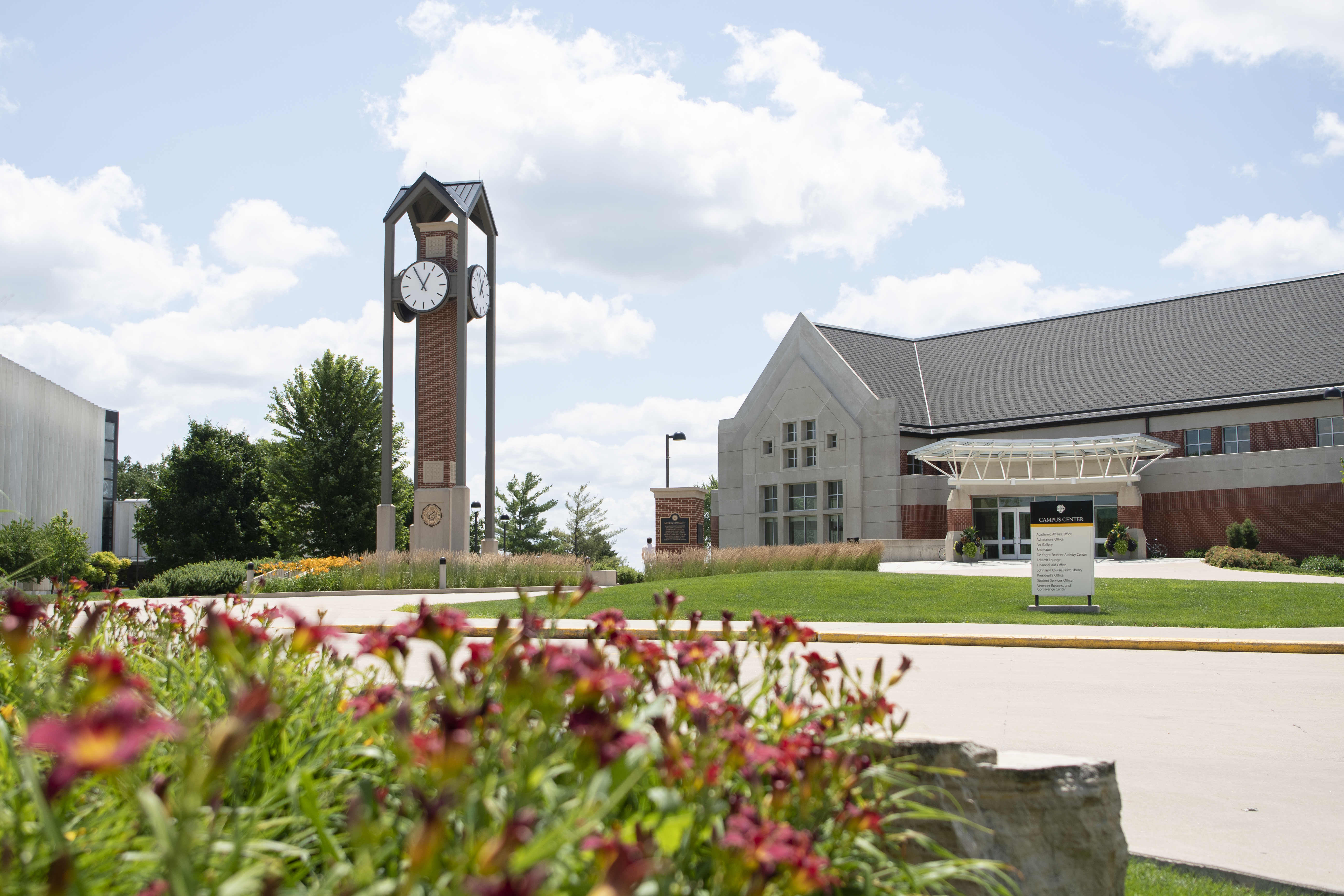 A view of Dordt's clocktower and campus center with flowers in the foreground.