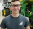 A student wearing safety glasses stands smiling in front of a tractor