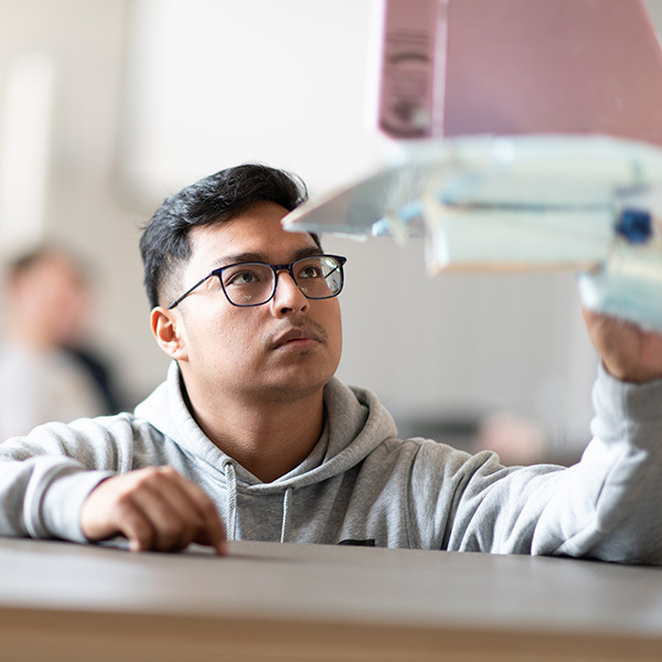 Young man with glasses looks up intently at model plane