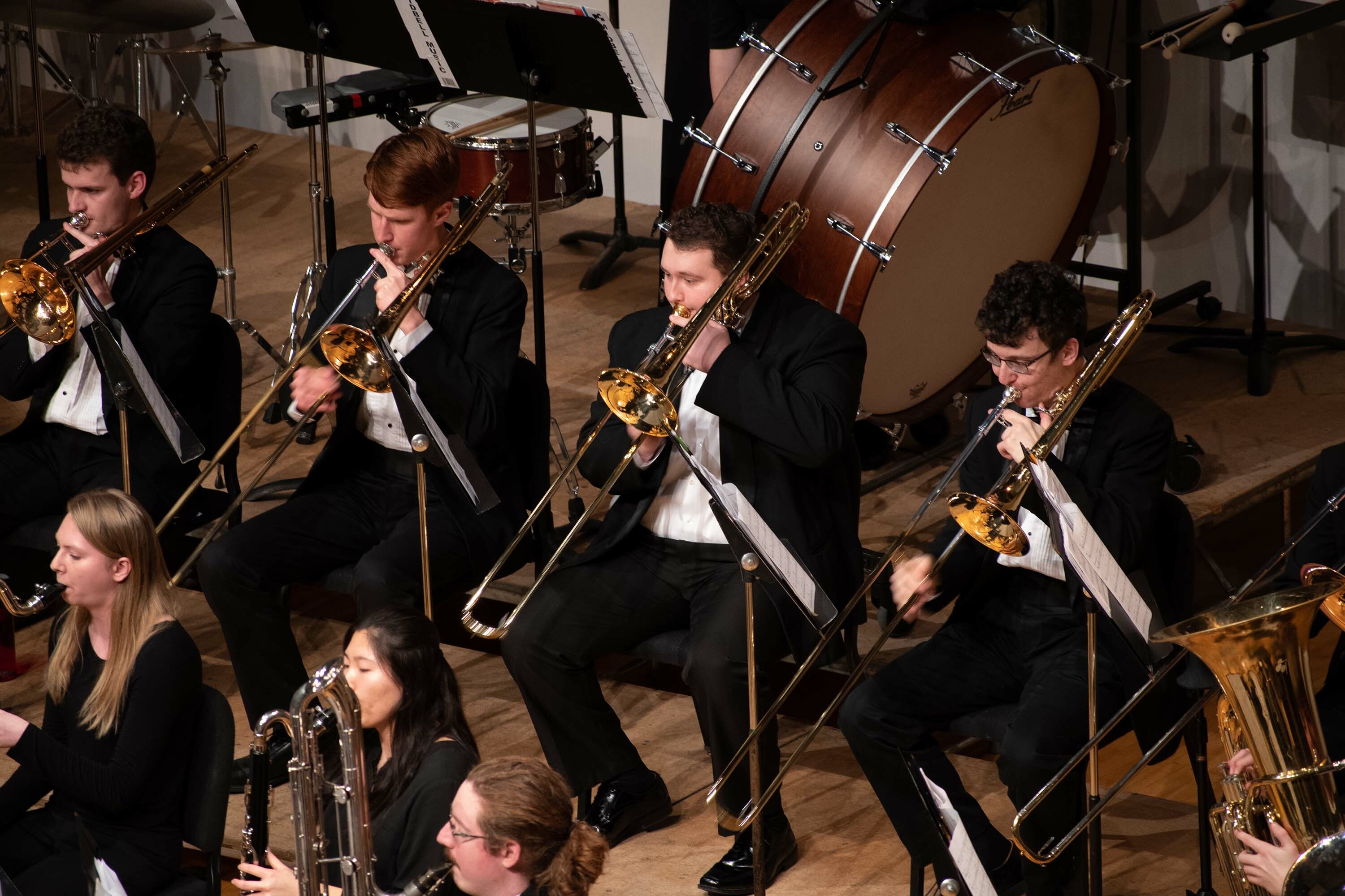 Three trombonists sit within the Wind Symphony ensemble playing