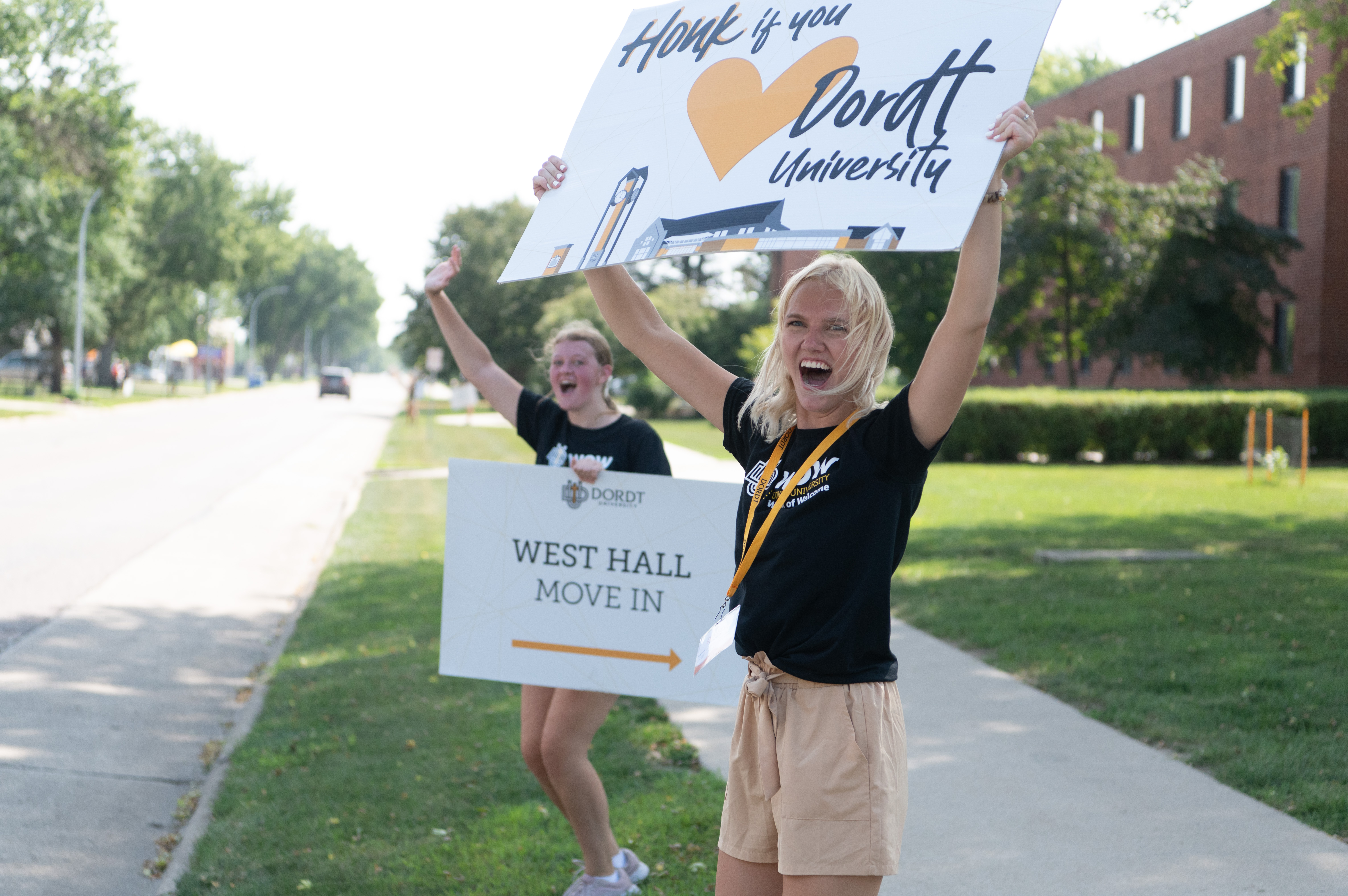 Two excited female students hold week of welcome signs