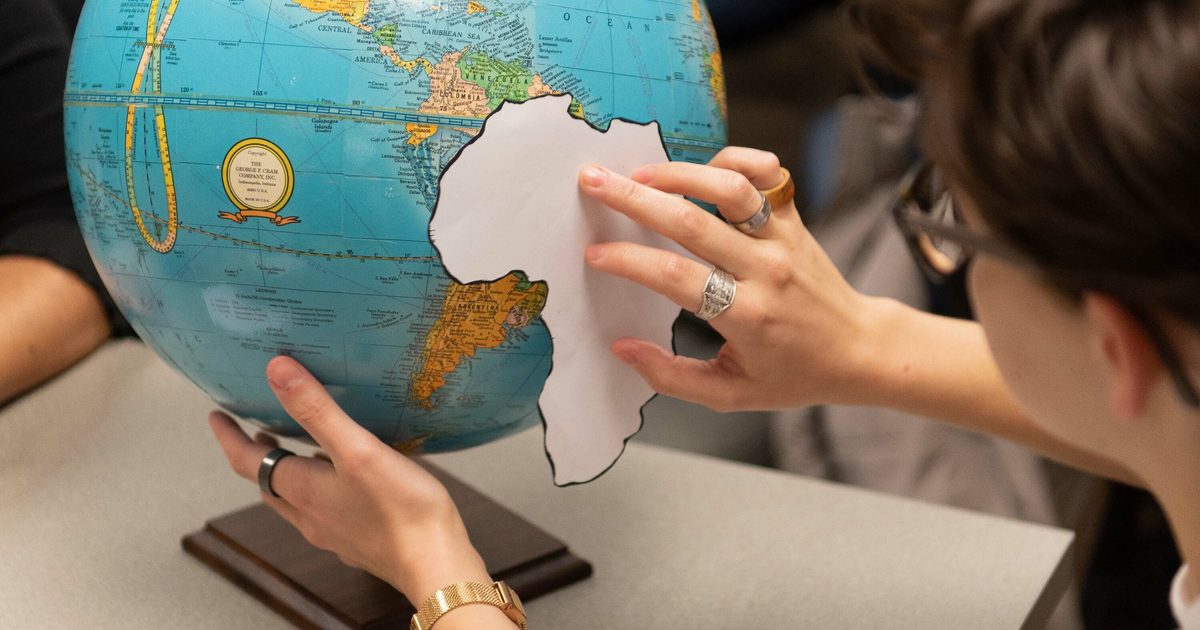 A student holds a paper cut out of the shape of Africa in front of a globe