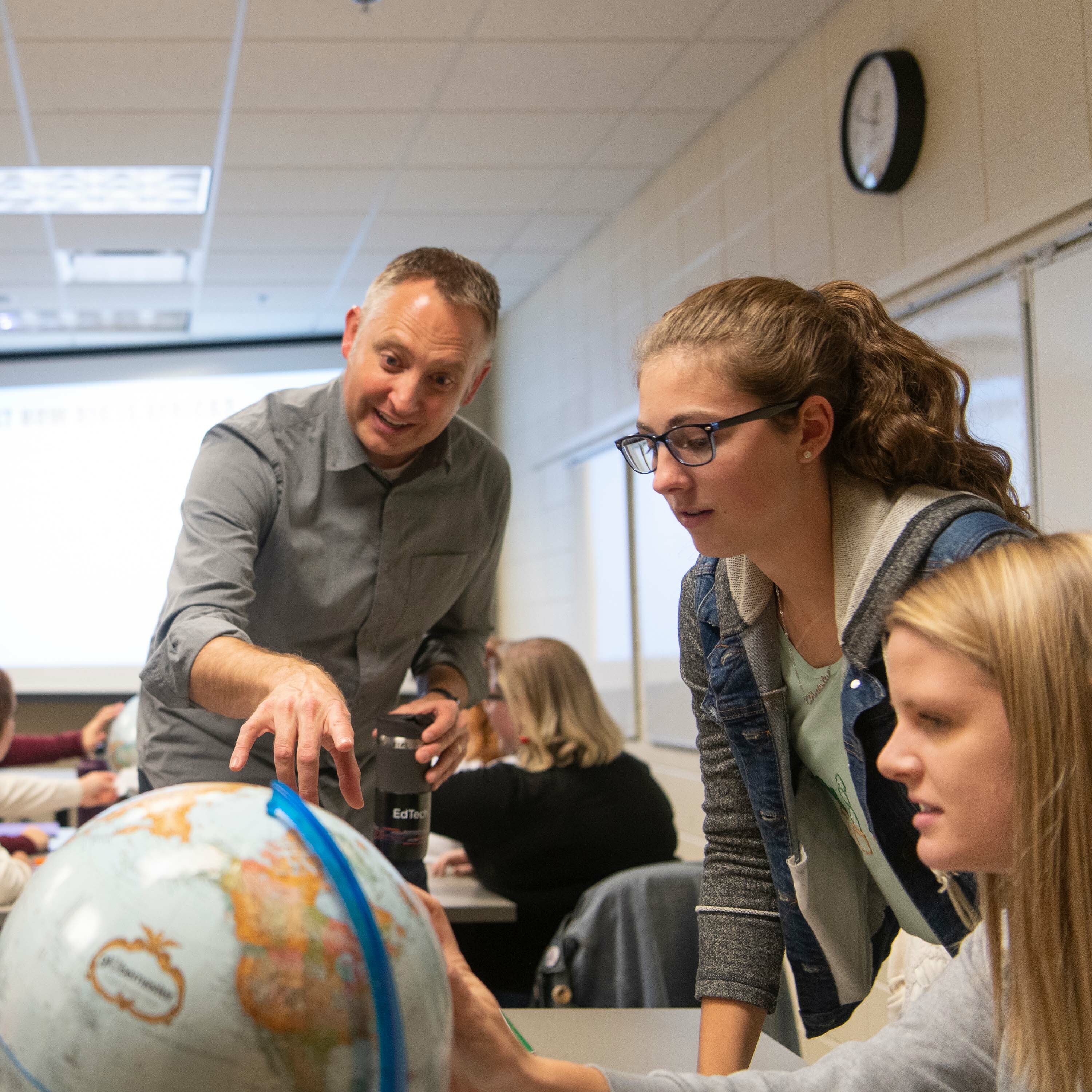 Dr. Mulder points to a globe as two students look on