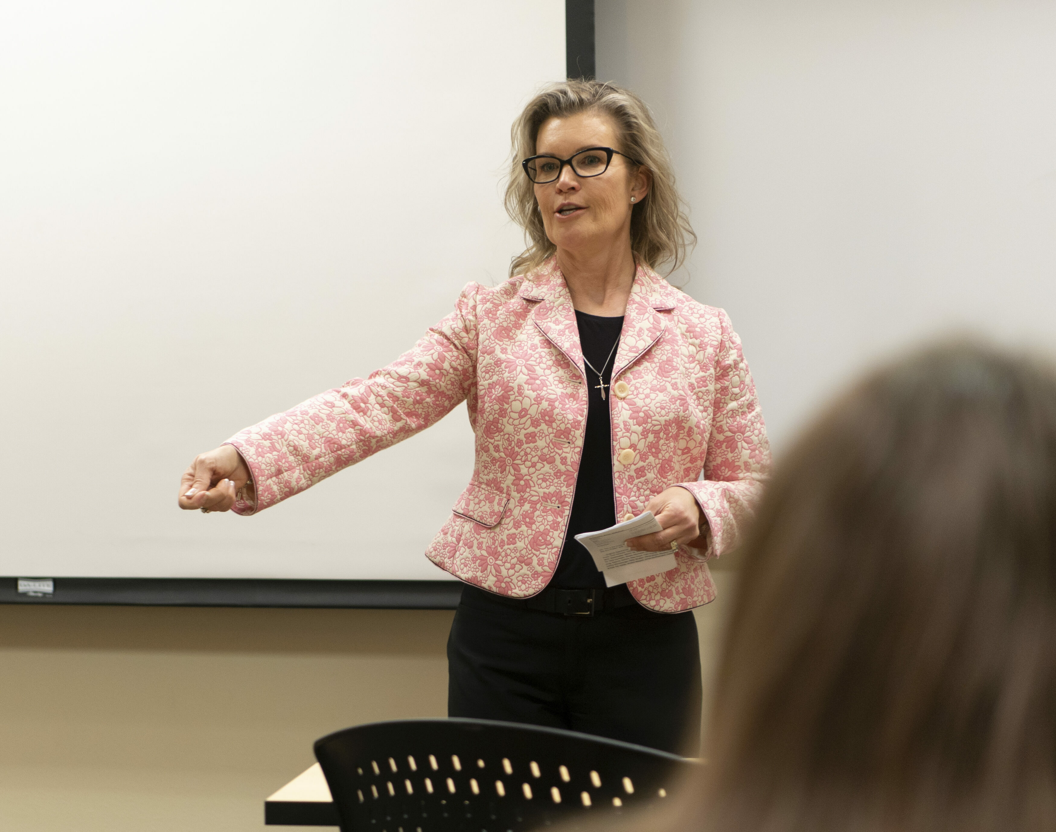 A professor in a pink jacket lectures to the class