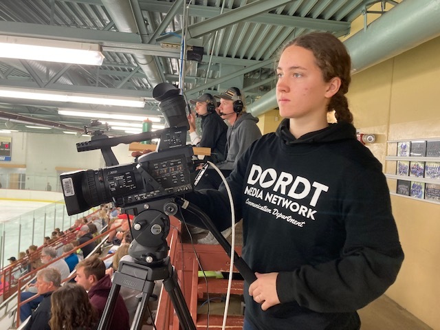 Female student works a camera for the Dordt Media Network at a hockey game
