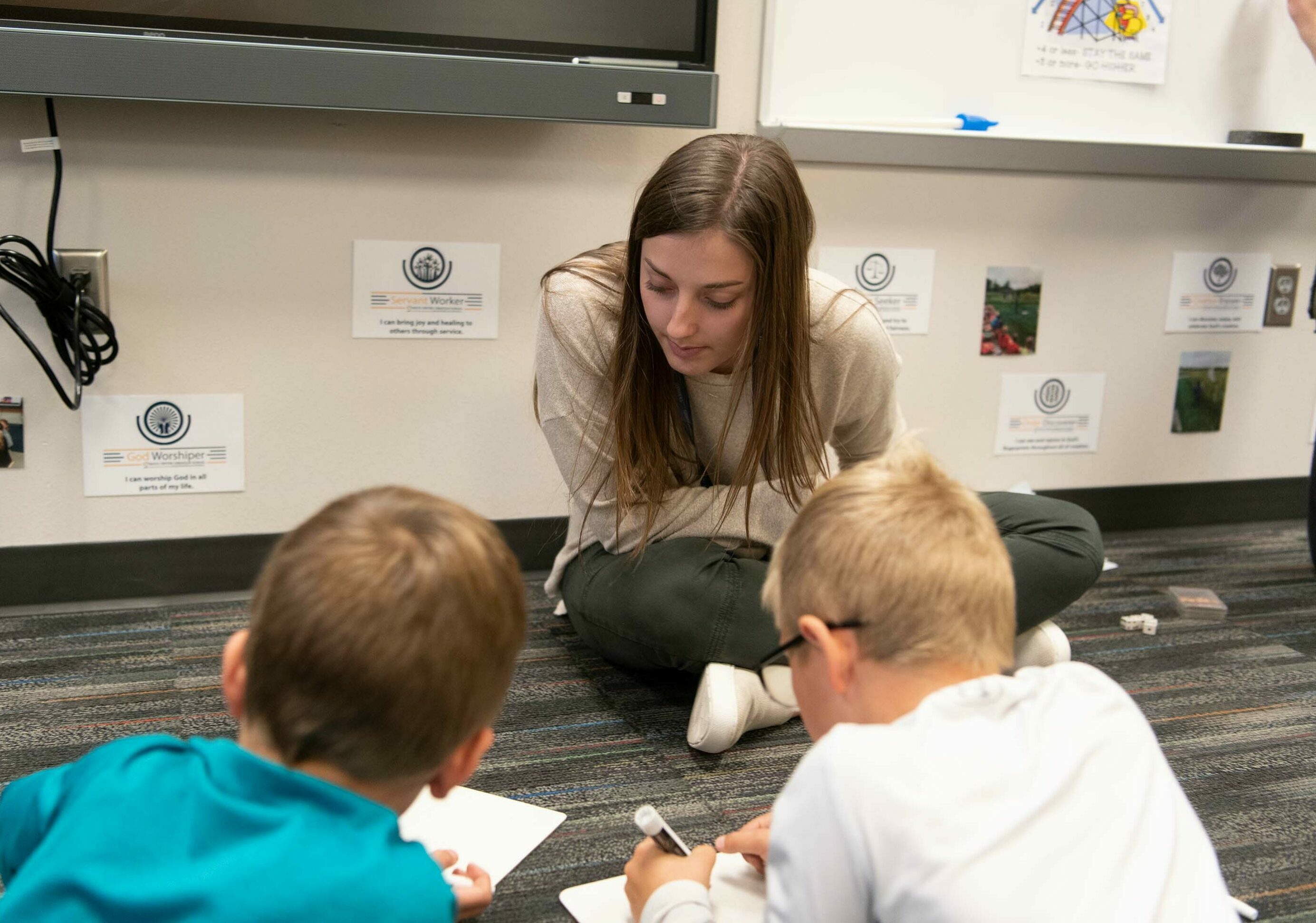 A Dordt student leans over two young students in class as they work on math