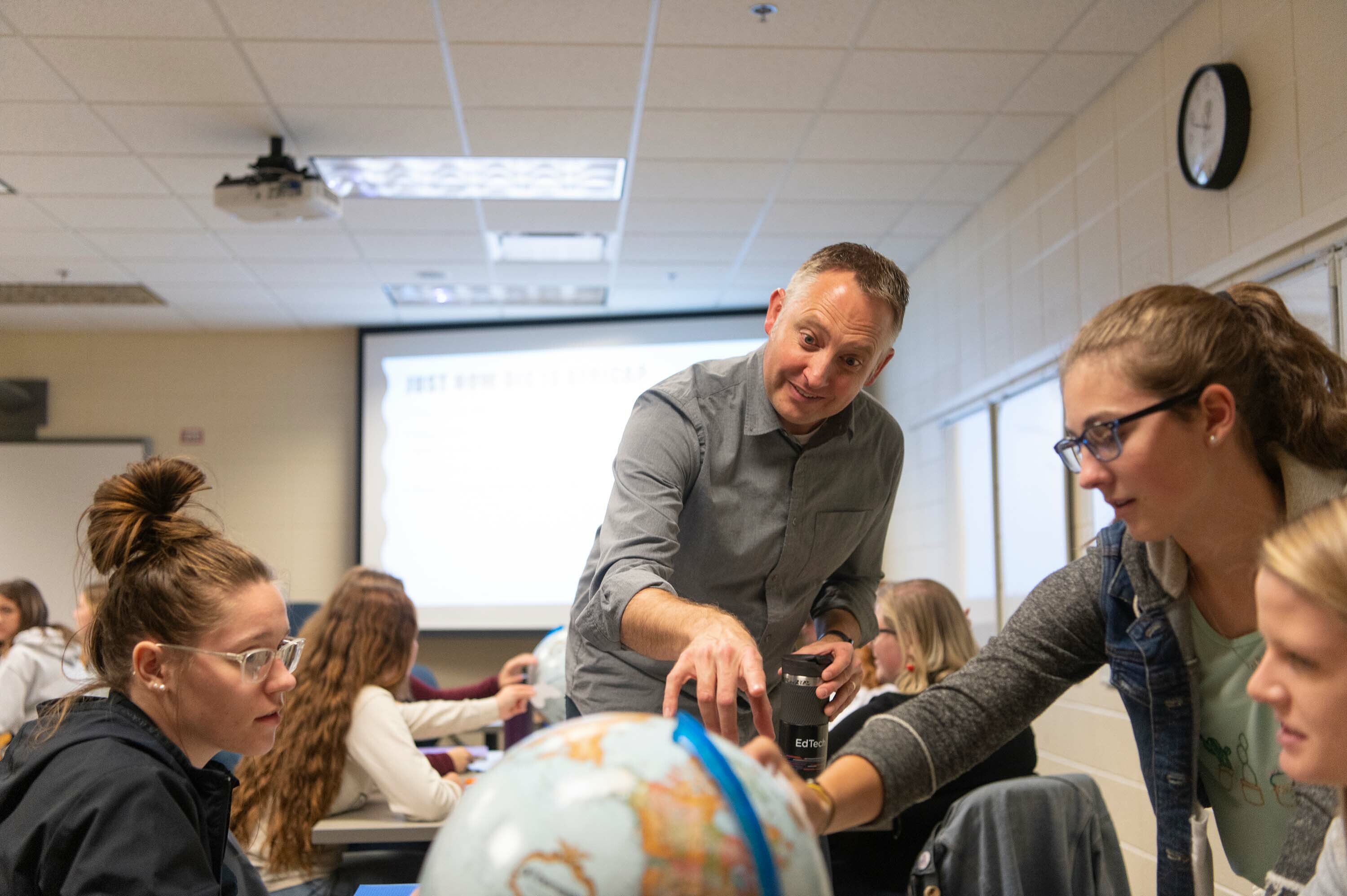 A Dordt professor points to a globe as Dordt students at a table look on