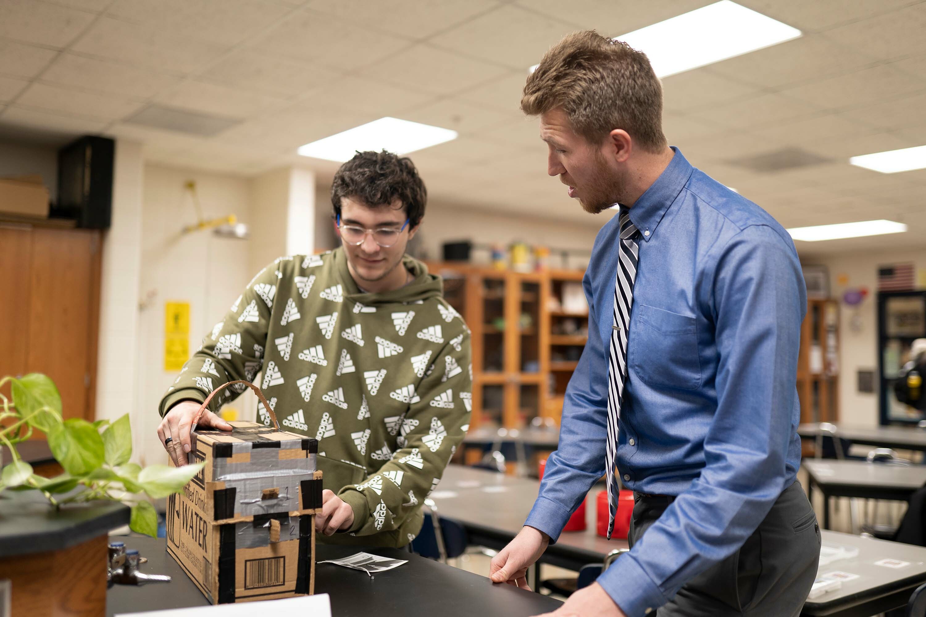 A male student teacher in the Professional Development School program works with a high school student in the classroom on a STEM project
