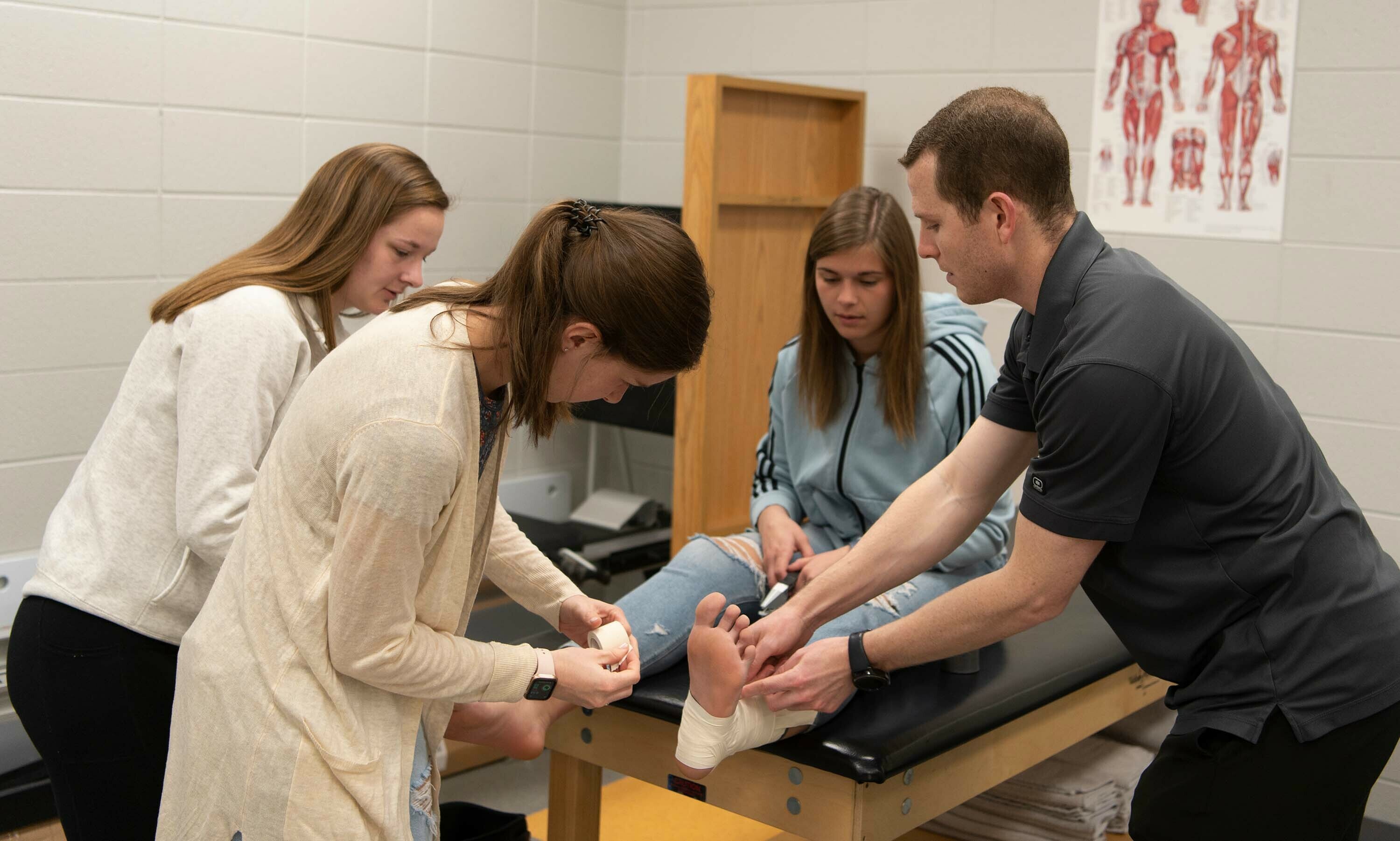A professor helps two students as they tape another student's ankle