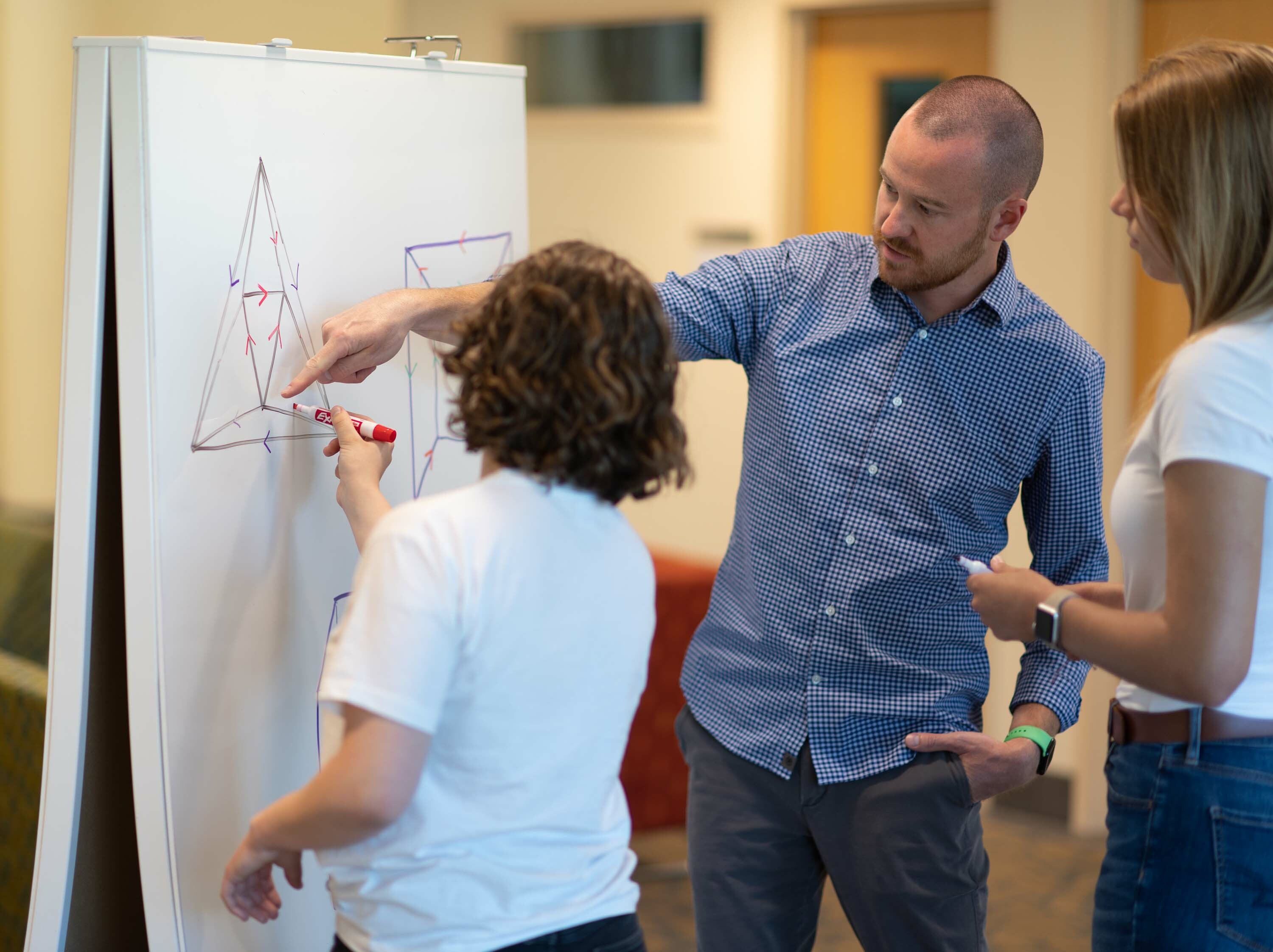 A professor and two students work on a diagram on a whiteboard