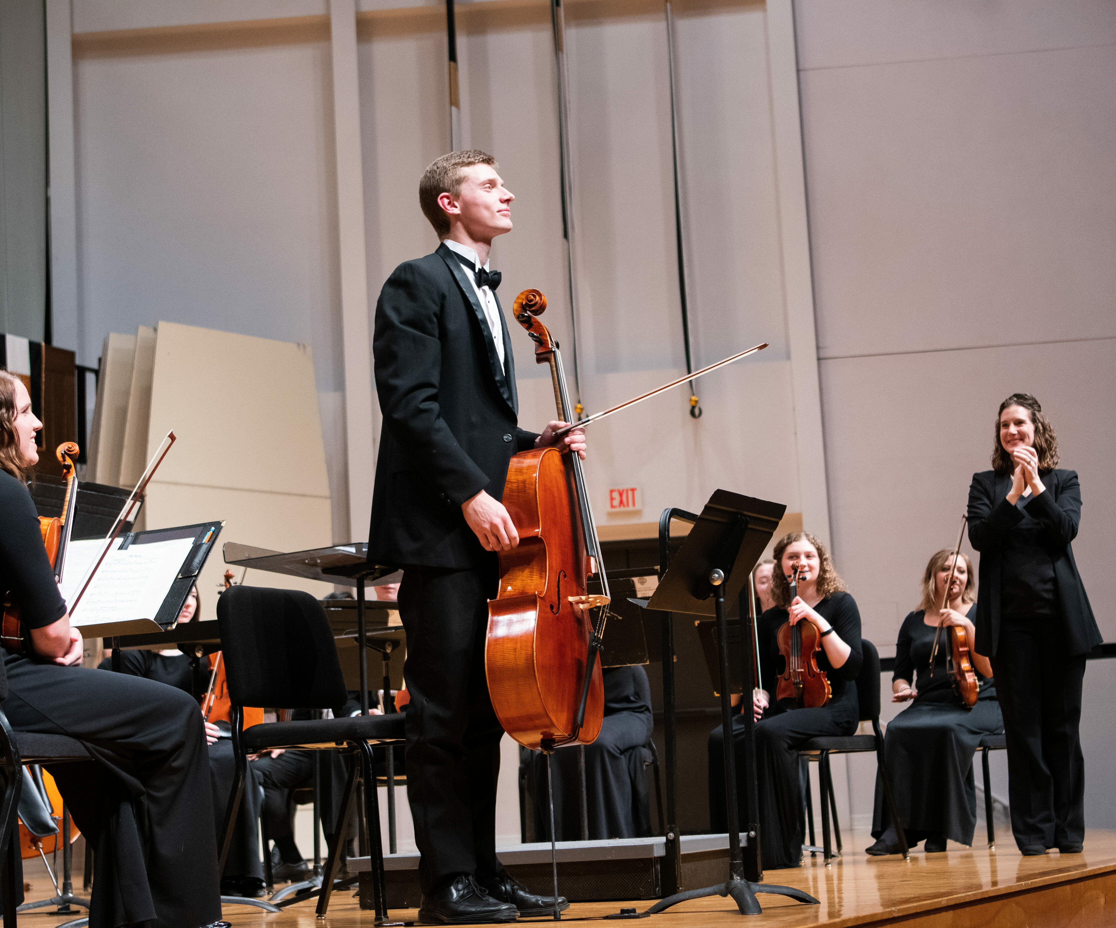 Male cellist stands before the orchestra on stage after completing a solo part