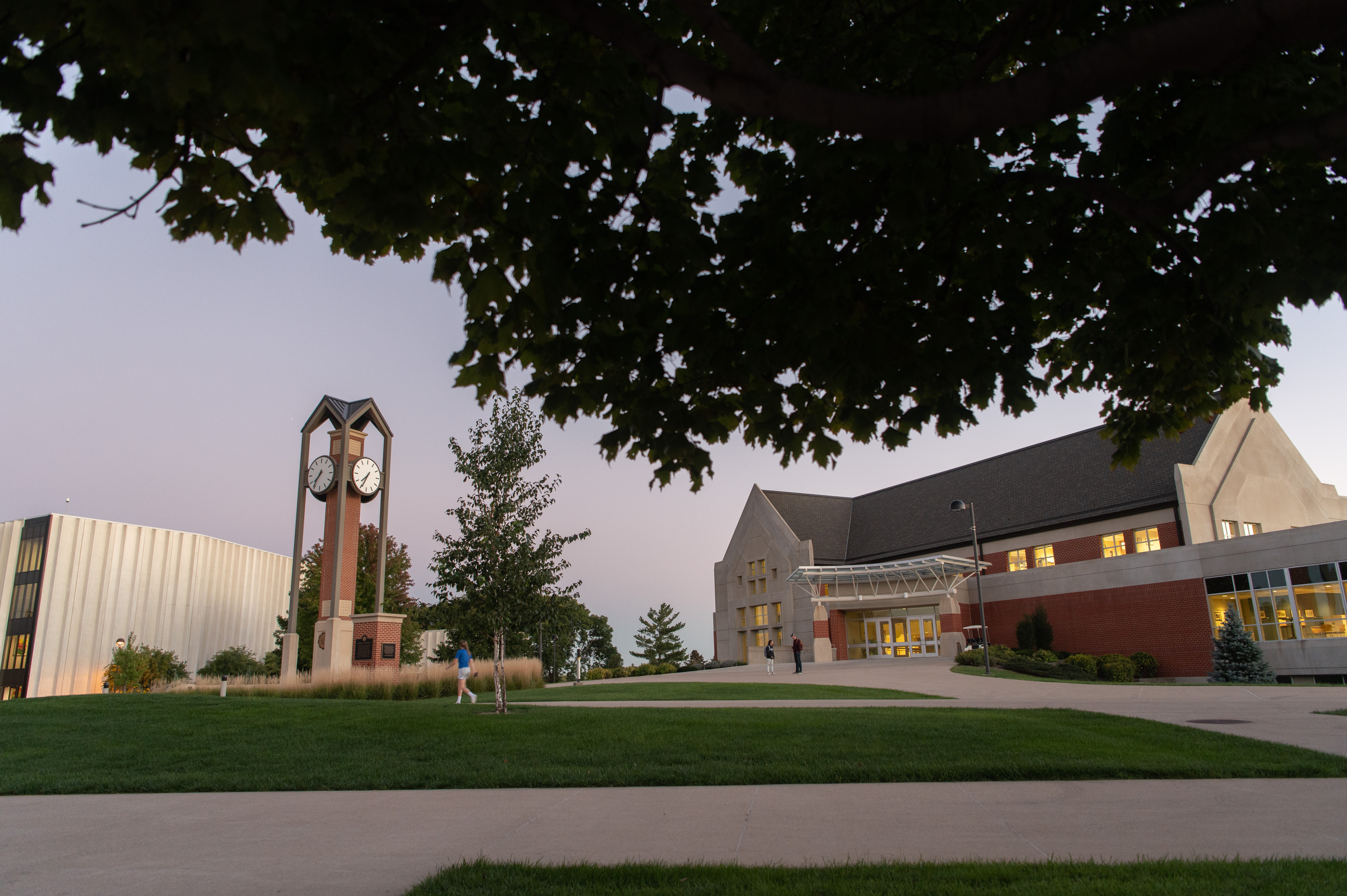 The Campus Center building and clocktower at dusk with overhanging tree in the top foreground