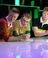Three young men in rugby shirts lean over counter on stage