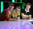 Three young men in rugby shirts lean over counter on stage