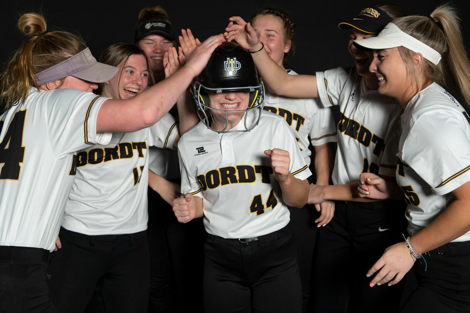 Dordt's softball team all hit their teammate who is wearing a helmet on the head