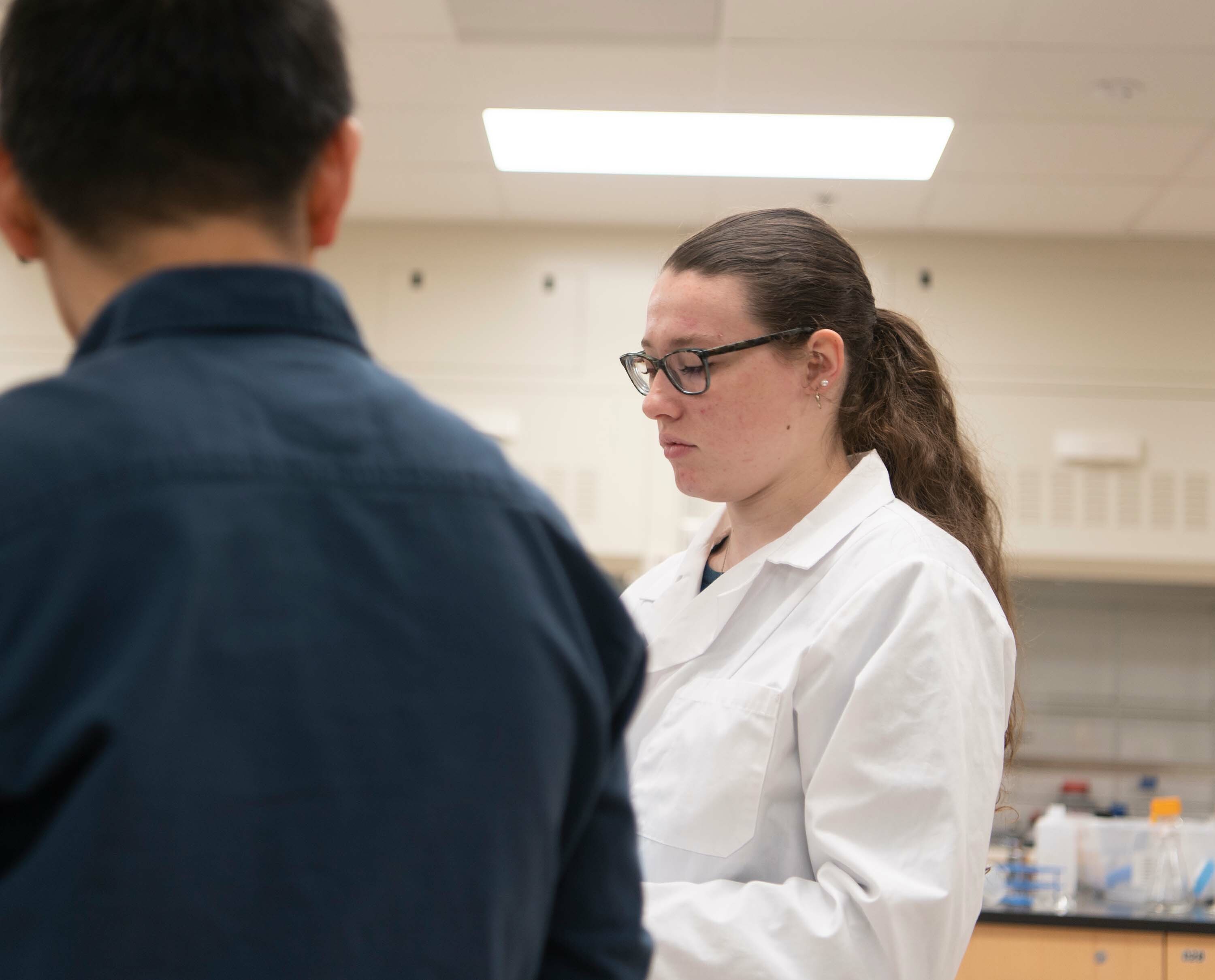 A student in a lab coat interacts with a professor in a lab