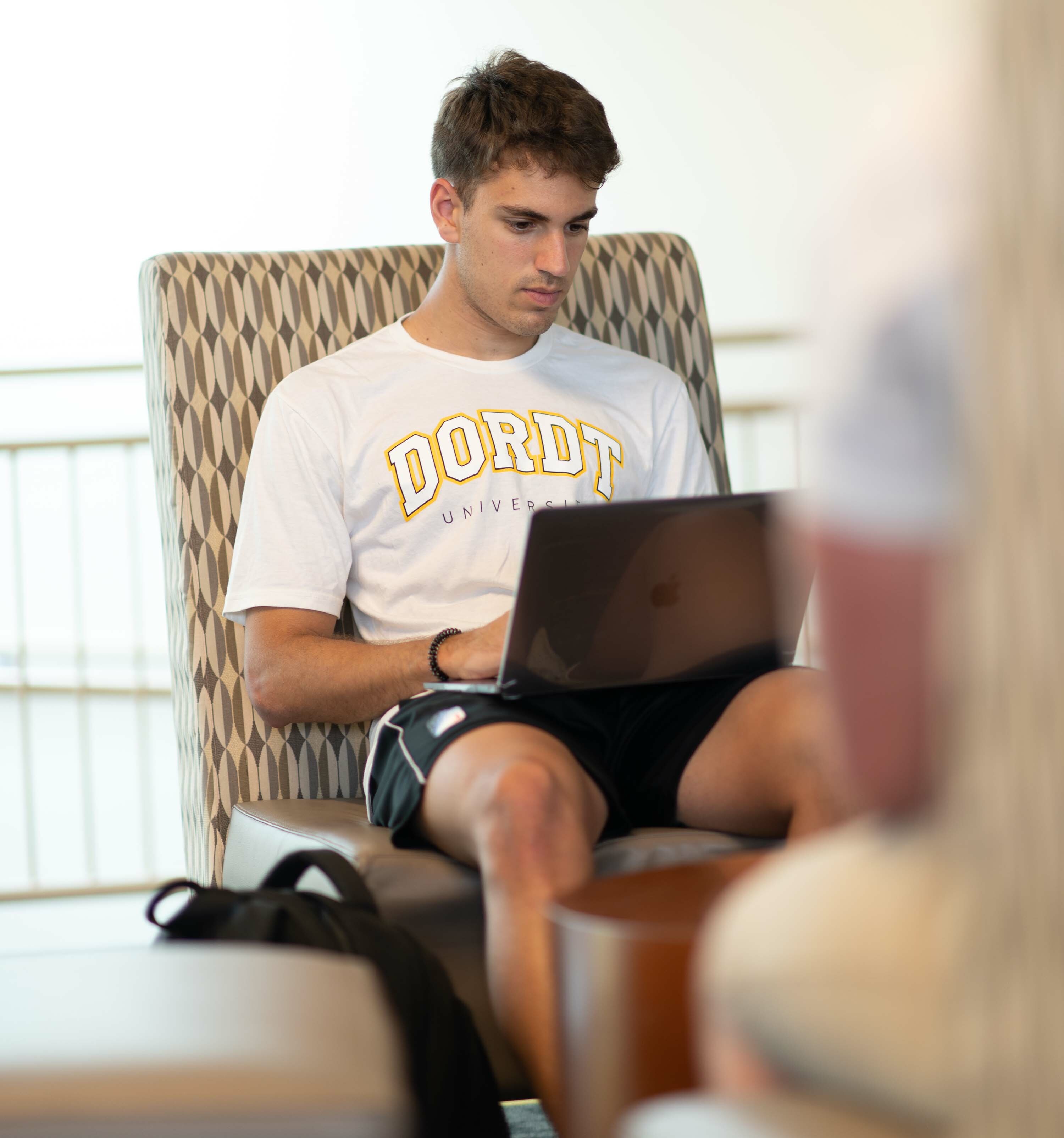 a male student sits in the lounge and types on his computer
