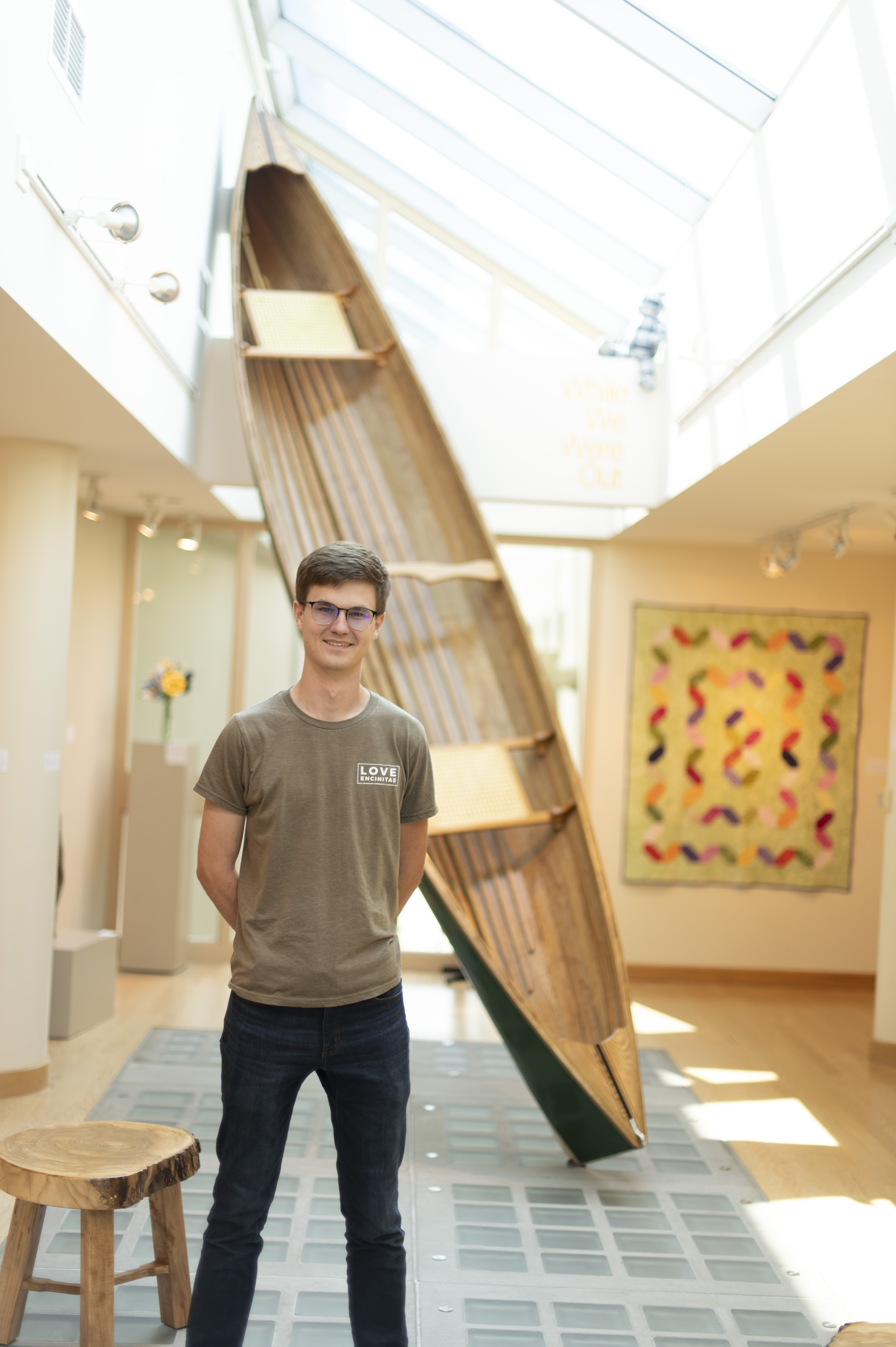 A male student stands in front of a giant canoe that he crafted.