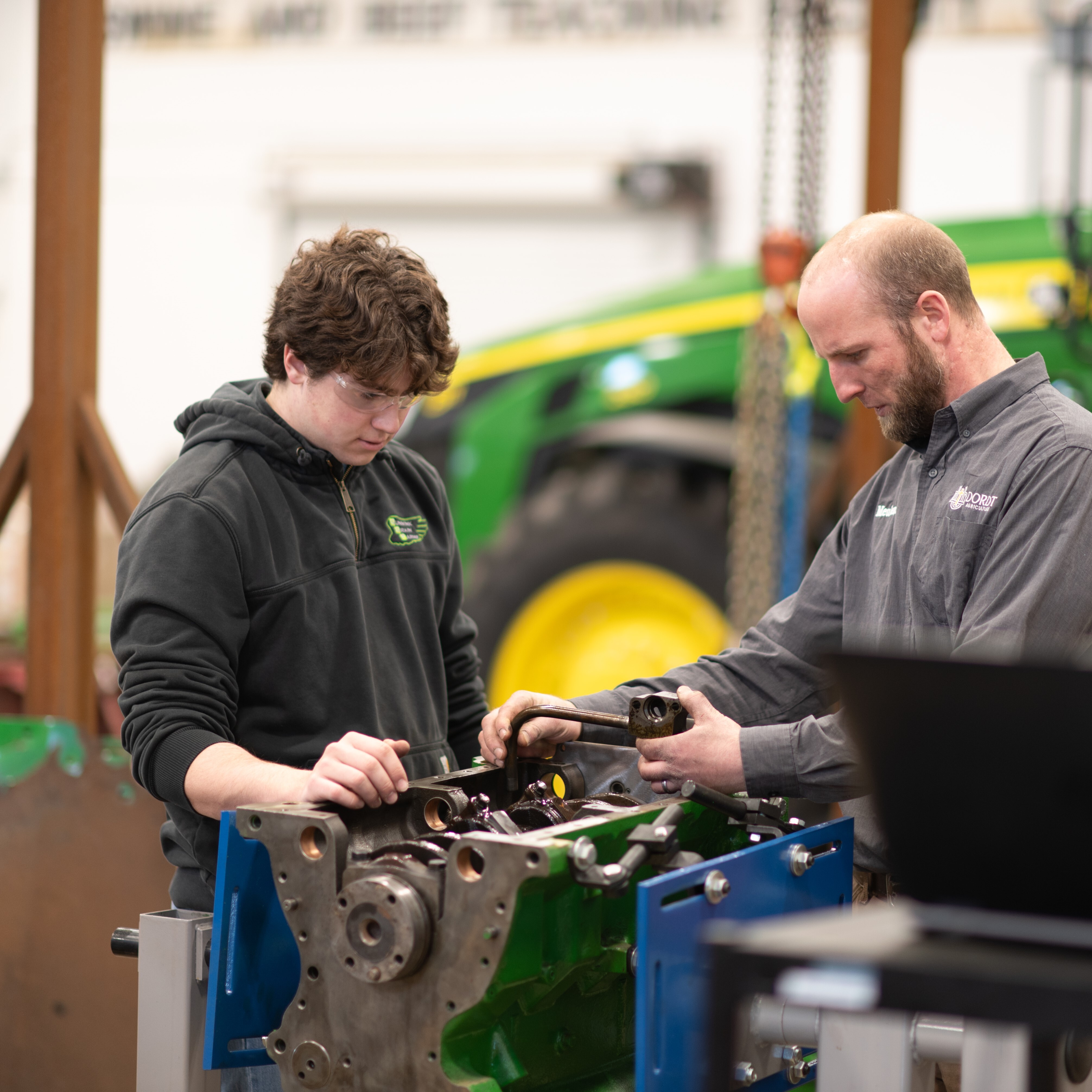 Male student working on tractor parts with teacher's assistance