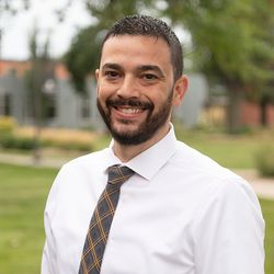 Smiling young man with dark hair and campus in the background