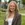 Blond-haired young woman in sport coat smiling in front of building