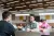 Young man at table converses with another young man in large space with expansive wood beams on ceiling