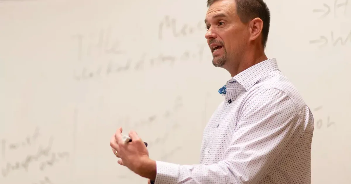 Middle-aged man lectures in front of whiteboard