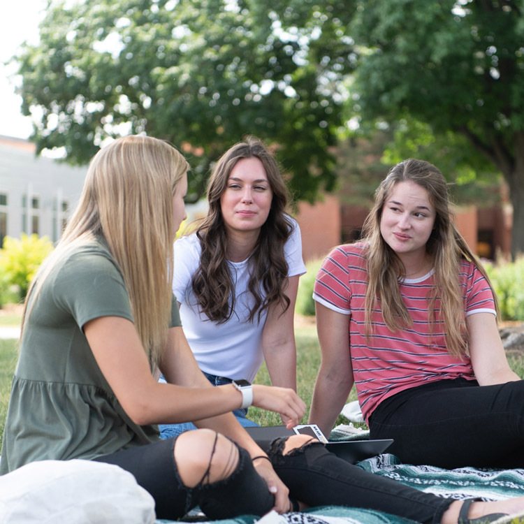 Three Dordt students sitting outside having a conversation