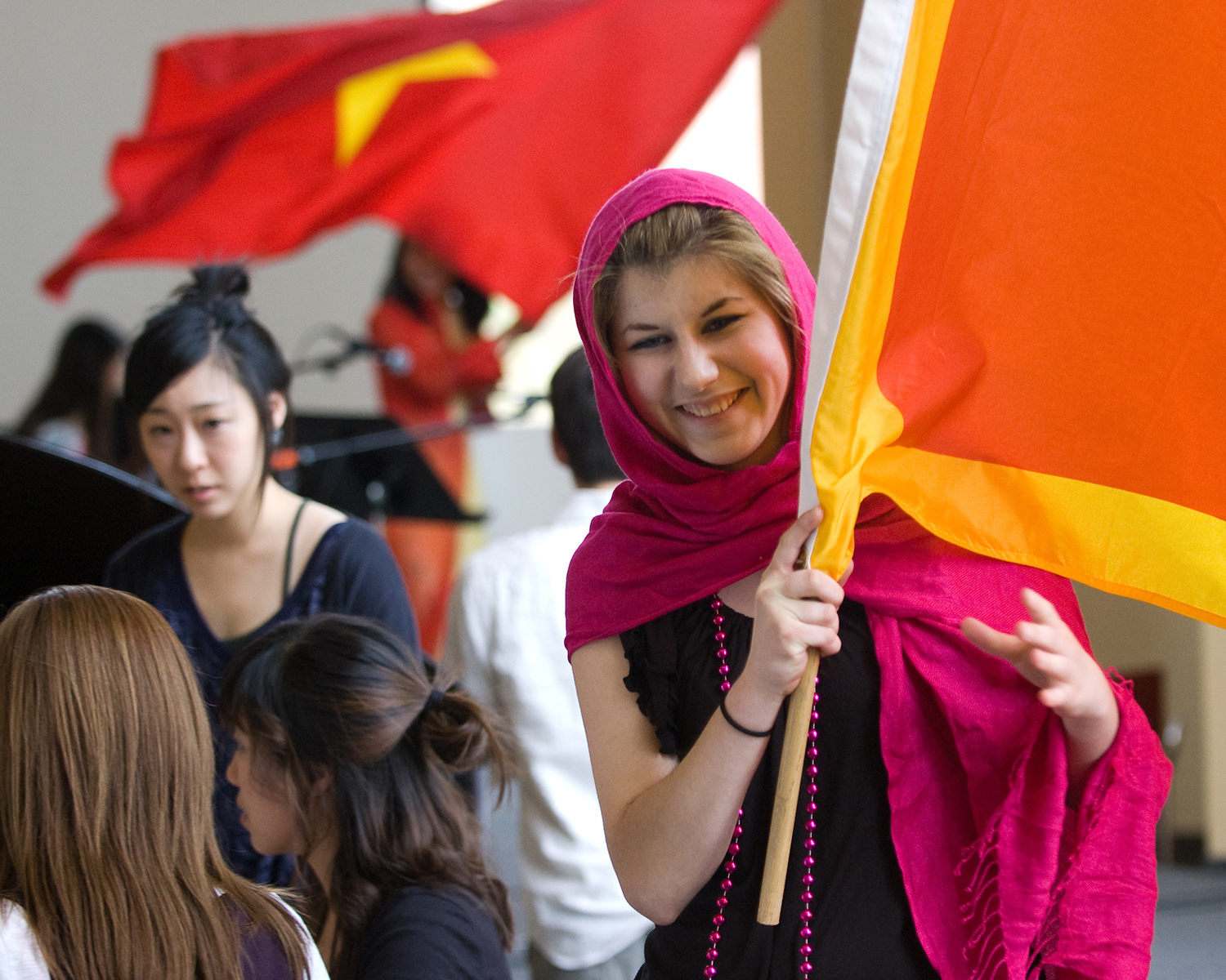 Female in pink hood holding flag while other international flag is displayed in background