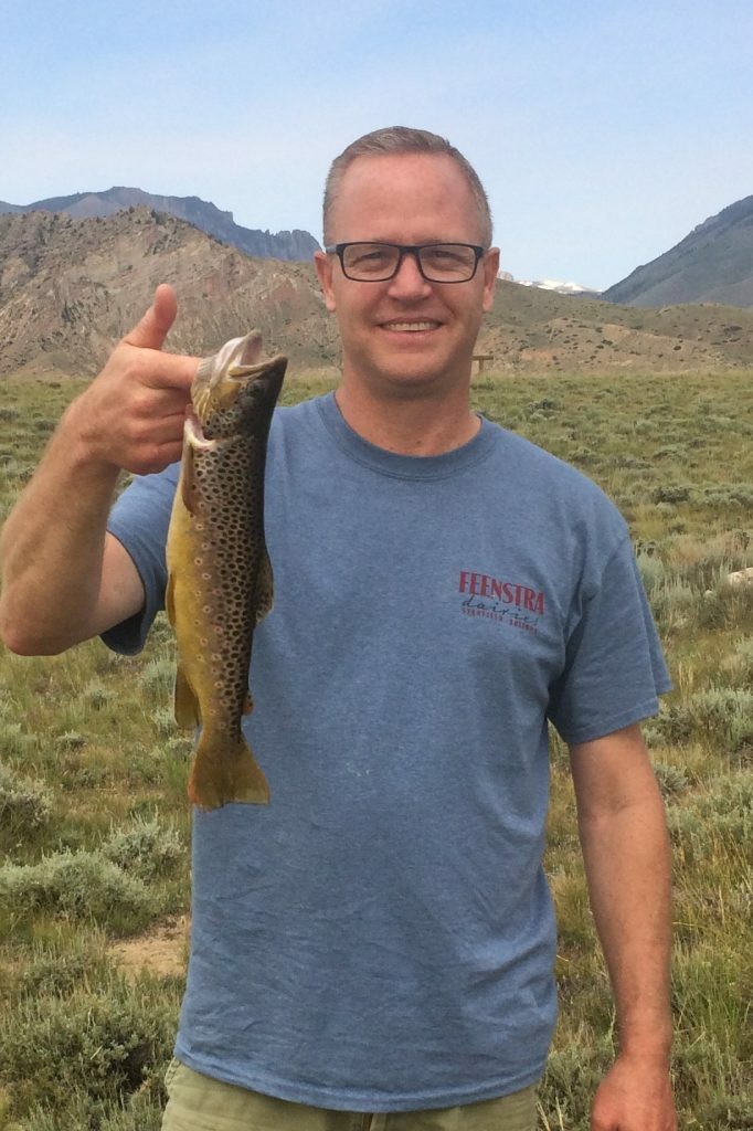 A picture of a man in a grayish-blue shirt holding a fish