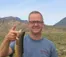 A picture of a man in a grayish-blue shirt holding a fish