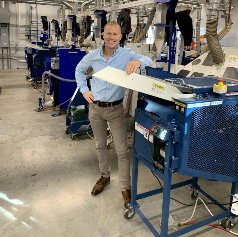 A picture of a man in a light blue shirt standing next to machinery