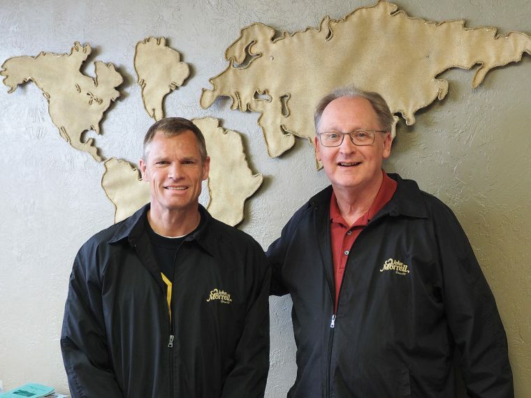 Two people in black jackets in front of a sketching of the world