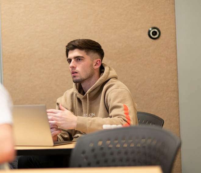 A Dordt student sitting at his desk looking at the front of the room with his laptop in front of him