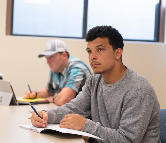 A dordt student looking up at his professor while writing in a notebook